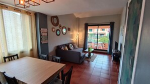 Un salon avec un canapé, une table à manger avec des chaises et un balcon offrant une vue sur les immebles.