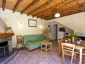 A cozy living room with a green sofa, a fireplace, a dining table with chairs, and a kitchen area with a microwave and stove.