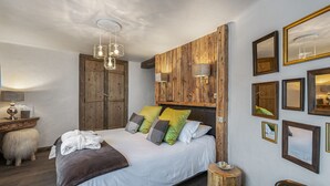A bedroom with a wooden headboard, a bed with multiple pillows, a nightstand, a lamp, and a mirror on the wall.