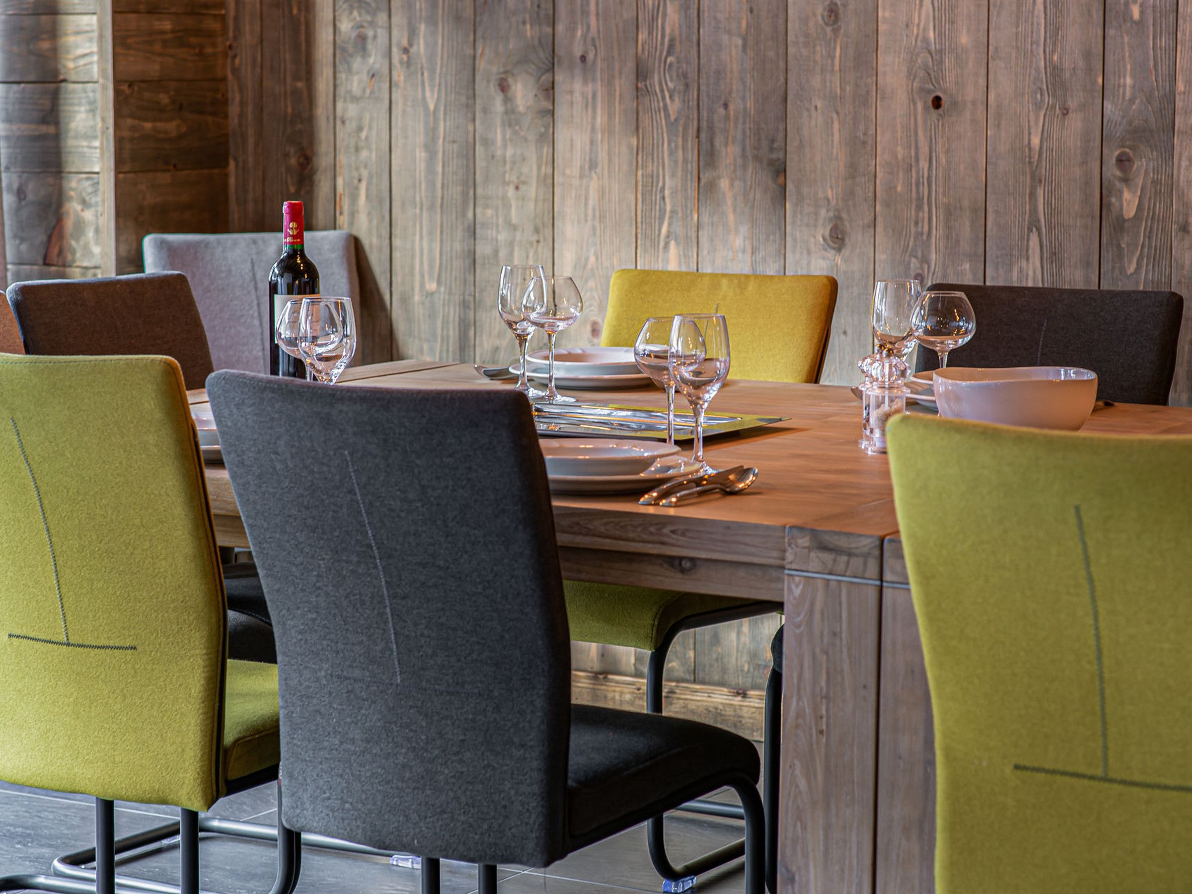 Mesa de comedor dispuesta con platos, vasos y cubiertos, rodeada de sillas de diseño moderno.