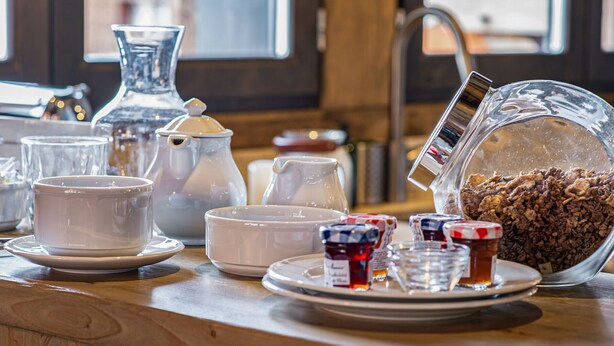 A dining table with various white ceramic dishes, a glass pitcher, and jars of jam.