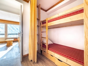 Dormitorio con literas, piso de madera, ventana con vistas a montañas nevadas y un banco de madera en el exterior.
