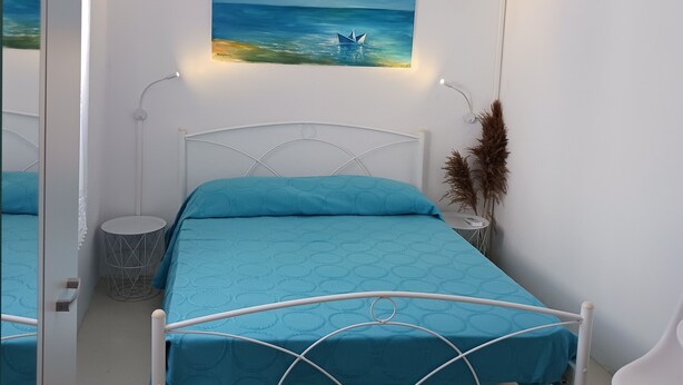 A bedroom with a bed, a small bedside table, a wall-mounted painting, and a mirror. - Cycladic Charming Studio in Mykonos (Mykonos)