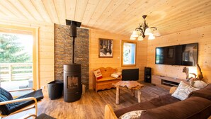 A cozy cabin interior with a wood-burning stove, a sofa, a TV, and a wooden ceiling. - Luxury Chalet with Spa, Near Ski Resorts, Sleeps 8 (Ban-sur-Meurthe-Clefcy)