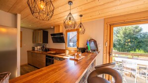 A modern kitchen with wooden countertops, a built-in oven, and a coffee machine. There is a bar area with a seating arrangement and a view of the outdoors. - Luxury Chalet with Spa, Near Ski Resorts, Sleeps 8 (Ban-sur-Meurthe-Clefcy)