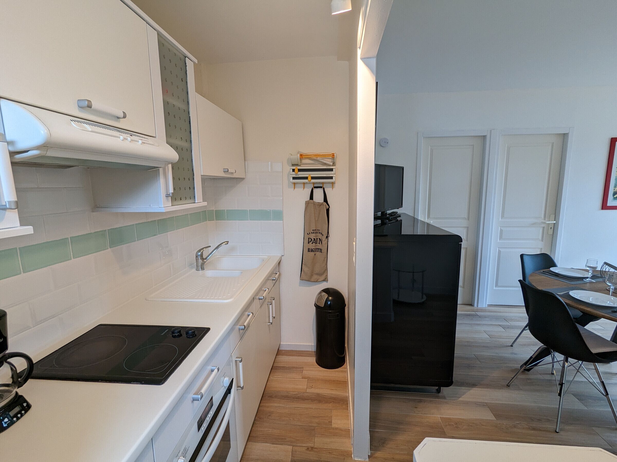A compact kitchen with a stove, sink, and cabinets. A dining area with a table and chairs is visible in the background.