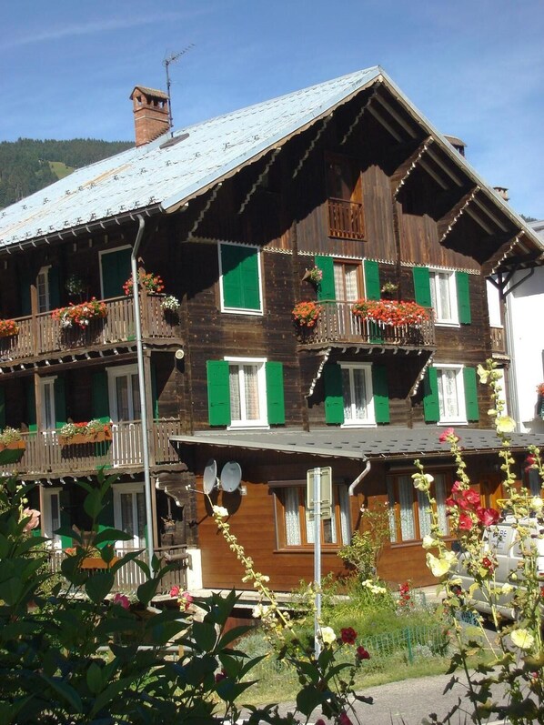 A multi-story wooden building with balconies, green shutters, and flower boxes.