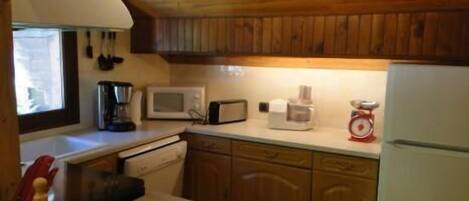A compact kitchen with wooden cabinets, a microwave, a toaster, and a refrigerator.