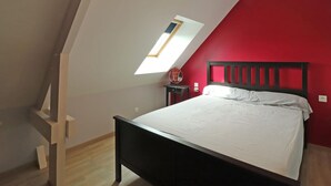 A bedroom with a sloped ceiling, a skylight, a bed, a nightstand, and a red wall. - Renovated house with enclosed garden, 3 bedrooms, free EV charging, near Swiss Normandy (Sainte-Opportune)
