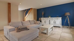 A living room with a grey sofa, a white coffee table, a white cabinet, a lamp, and a staircase. - Renovated house with enclosed garden, 3 bedrooms, free EV charging, near Swiss Normandy (Sainte-Opportune)
