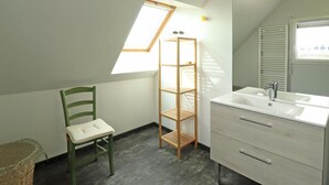 A small, modern bathroom with a skylight, a wooden shelf, a green chair, and a white vanity with a mirror. - Renovated house with enclosed garden, 3 bedrooms, free EV charging, near Swiss Normandy (Sainte-Opportune)