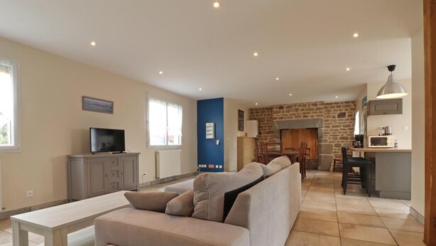A modern living room with a sofa, a TV, and a dining area with a stone fireplace. - Renovated house with enclosed garden, 3 bedrooms, free EV charging, near Swiss Normandy (Sainte-Opportune)