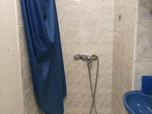 Un angolo doccia con tenda blu, soffione a mano e bacinella blu.