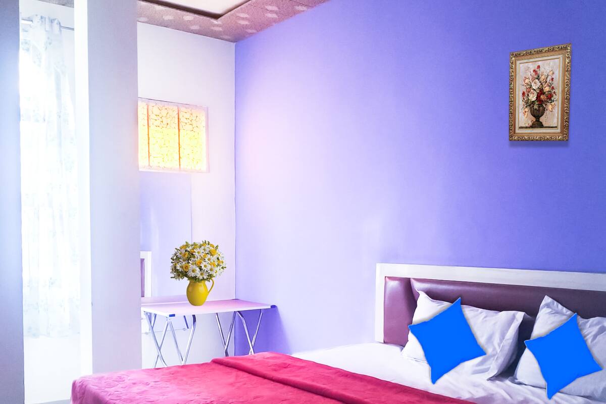 A bedroom with a bed, a nightstand, a vase with flowers, and a framed picture on the wall.