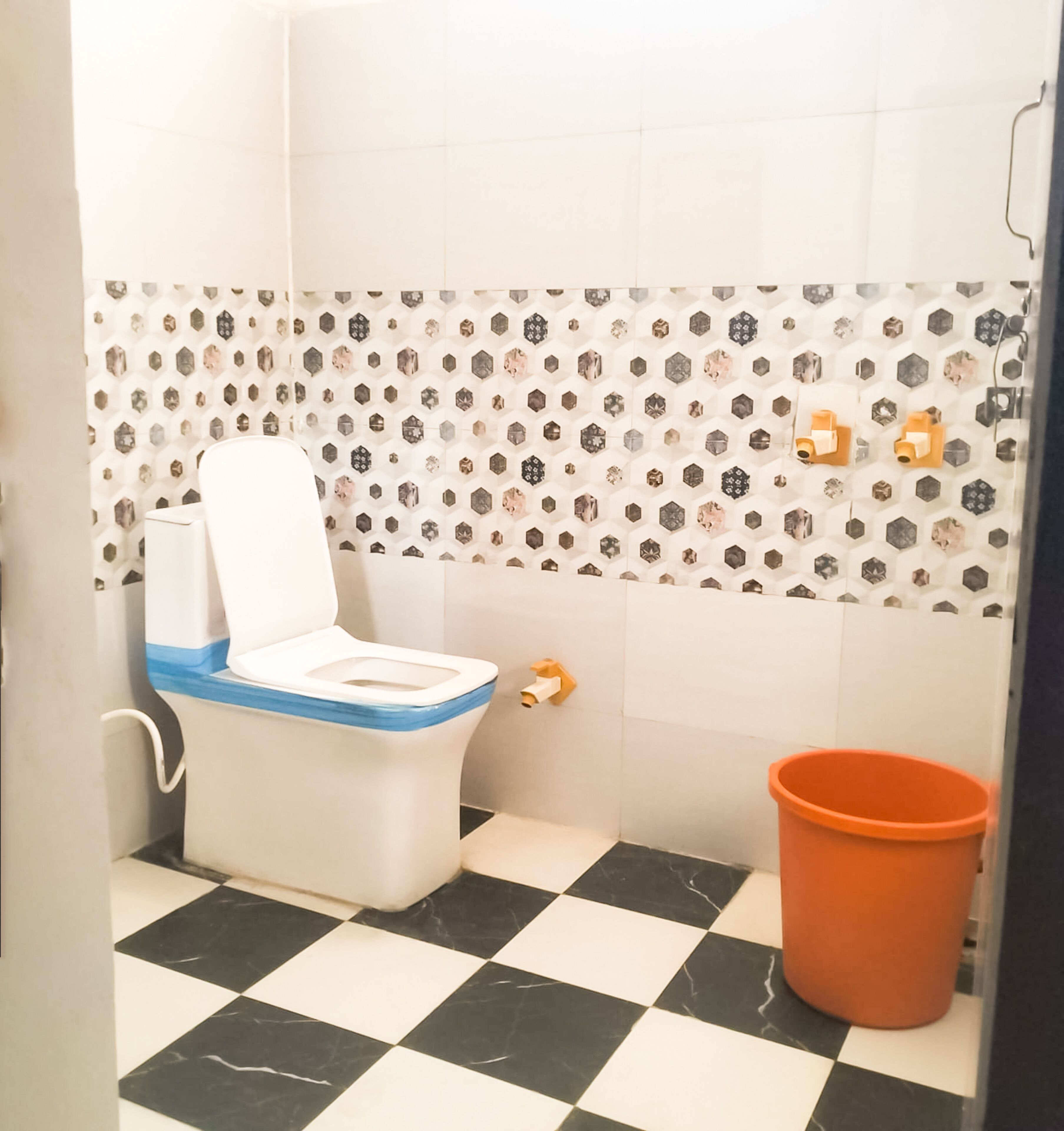 A small bathroom with a toilet, a checkered floor, and a tiled wall with hexagonal patterns.