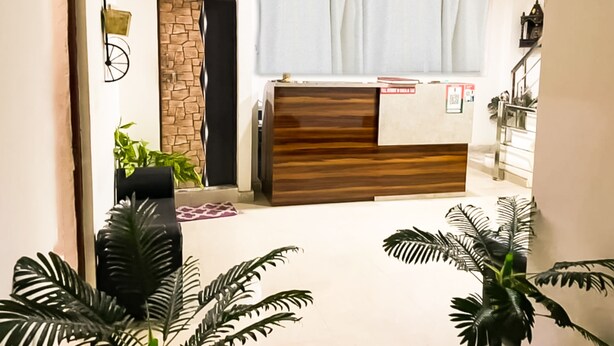A reception area with a wooden reception desk, a stone accent wall, and potted plants. - Roomshala 021 Hotel Joyous Inn (Ghaziabad)