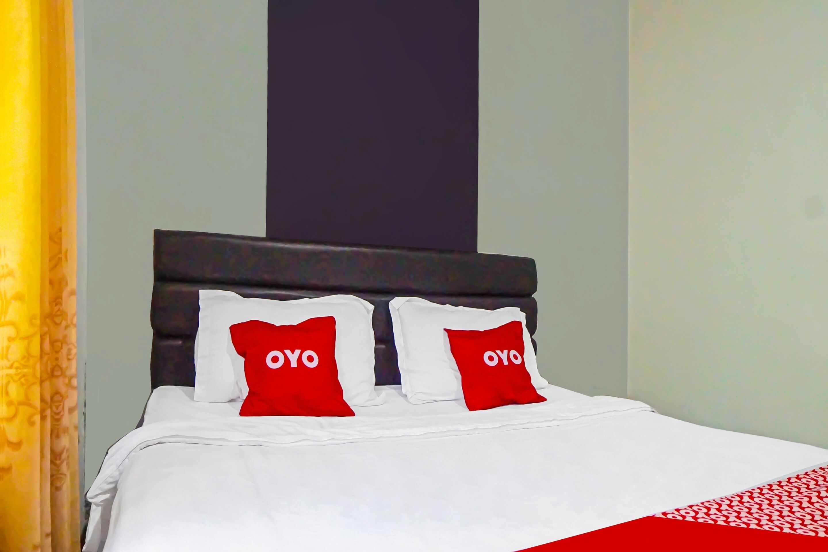 Una cama bien hecha con ropa blanca y dos almohadas rojas con el logo "OYO".