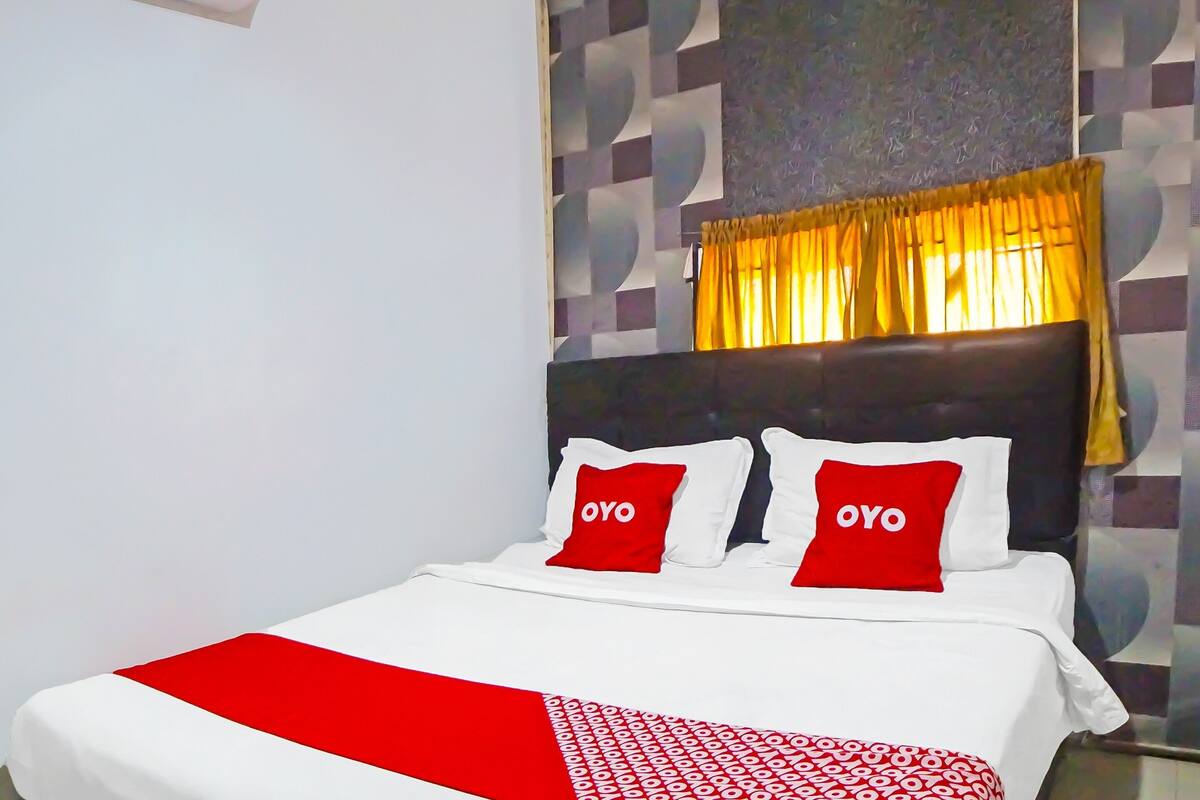 Hotellihuone, jossa on sänky, sängynpääty ja ikkuna, jossa on keltaiset verhot.