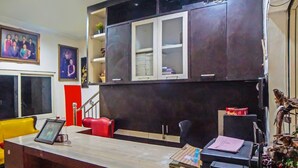 A reception desk with a framed photo, a red chair, and a bookshelf with decorative items. - Hotel O Abadi Hotel (Medan)
