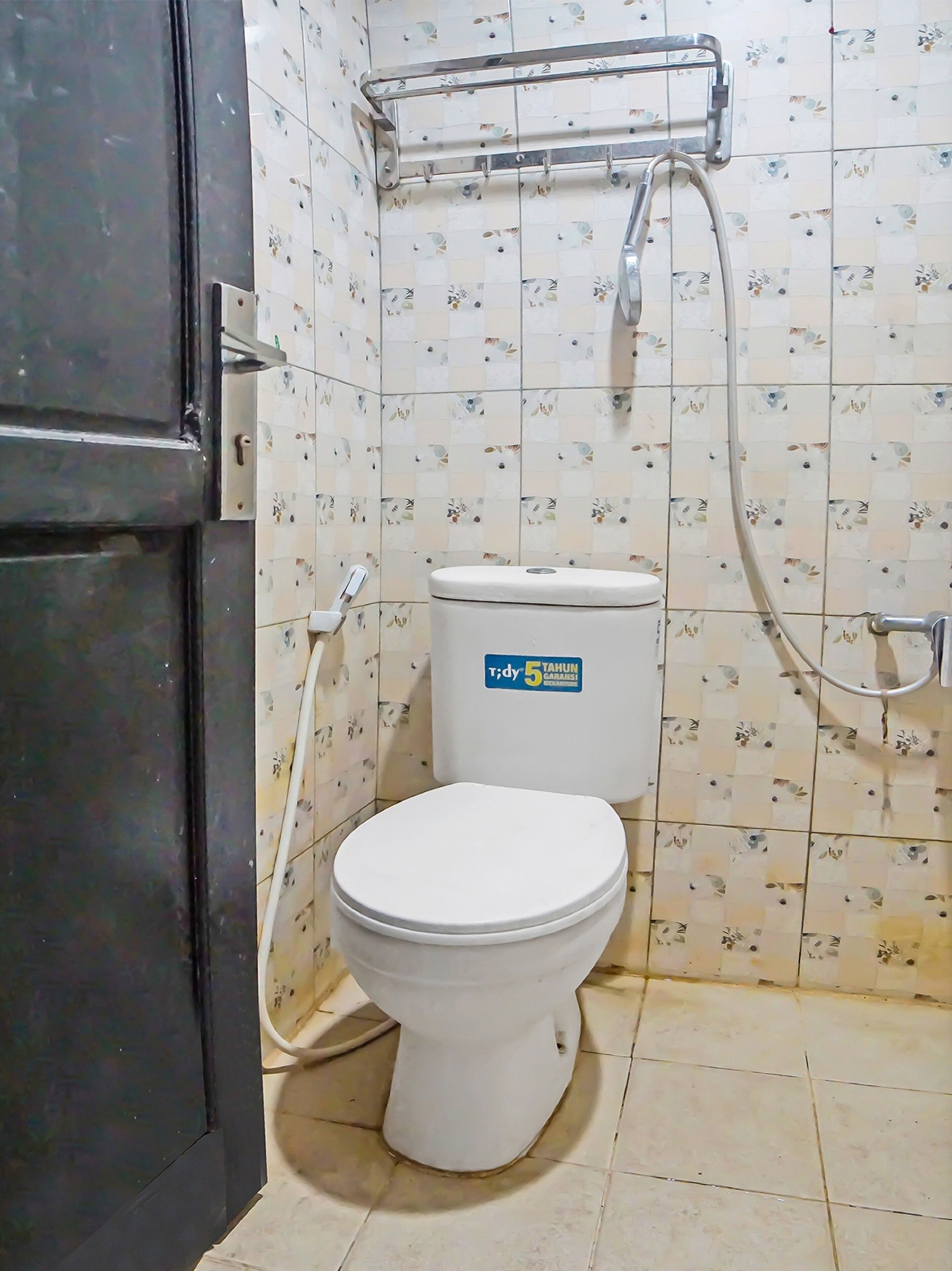 Egy kis fürdőszoba, amelyben WC, zuhanyzó és törölközőtartó található.