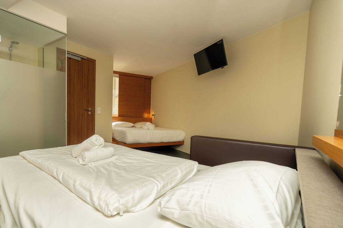 Une chambre d’hôtel avec deux lits, un téléviseur fixé au mur et une porte en bois.