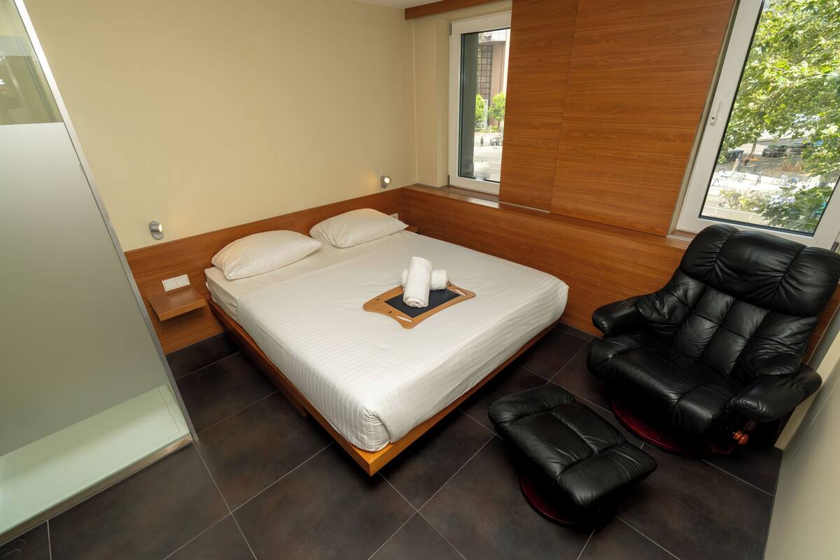 Une chambre moderne dotée d’un grand lit, d’un fauteuil massant et offrant une vue sur l’extérieur par une fenêtre.