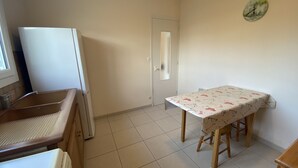Une cuisine équipée d’un évier, d’un réfrigérateur, d’une table à manger avec des chaises et d’une horloge au mur.