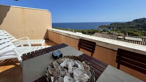 A balcony with a table set for dining, overlooking a scenic view of the sea and a hilly landscape. - Apartment in Aiguablava with Pools and Wifi (Begur)