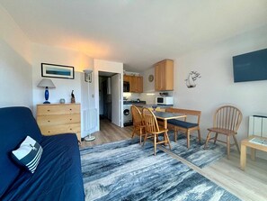 Ein kompakter Wohnraum mit Bett, Essbereich mit Stühlen, Küche mit Holzschränken und einem kleinen Tisch.