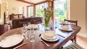 A dining area with a wooden table set for four, surrounded by chairs. - The Cow Barn - sleeps 6 guests  in 3 bedrooms (Banningham)