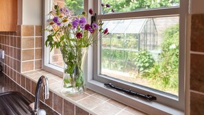 A kitchen with a window, a vase with flowers, and a view of greenery outside. - The Cow Barn - sleeps 6 guests  in 3 bedrooms (Banningham)