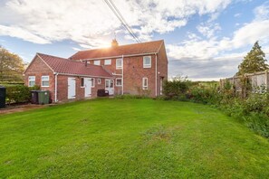 A two-story brick house with a red-tiled roof, a front door, and a small front yard with a lawn and a wooden fence. - No 2 , Sparham Hall  - sleeps 5 guests  in 3 bedrooms (Swaffham)