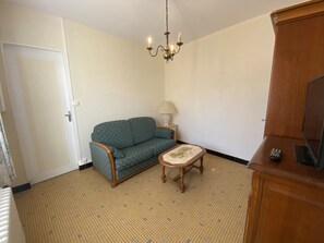 A room with a patterned floor, a sofa, a small table with a lamp, a television, and a wooden cabinet.
