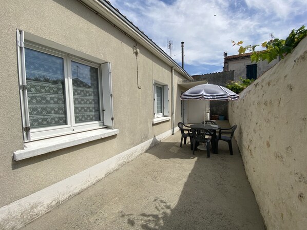 A small outdoor patio with a table and chairs, a striped umbrella, and a white wall.