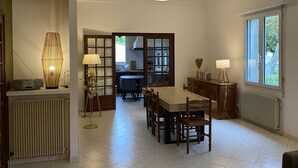 A spacious dining area with a wooden table and chairs, a modern pendant light, and a view of the kitchen through a glass door.