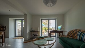 Ein geräumiges Wohnzimmer mit einem grünen Sofa, einem Esstisch und einem großen Fenster mit Blick ins Freie.