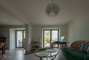 Ein geräumiges Wohnzimmer mit einem grünen Sofa, einem Esstisch und einem großen Fenster mit Blick ins Freie.