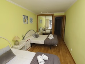 A hotel room with two beds, a bedside table with a lamp, a mirror, and artwork on the wall.