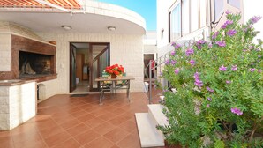 Une terrasse avec une cheminée en pierre, une table à manger décorée de fleurs rouges et un escalier menant à un niveau supérieur.