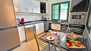 Una cocina moderna con armarios blancos, microondas integrado y un comedor con una mesa preparada para dos.