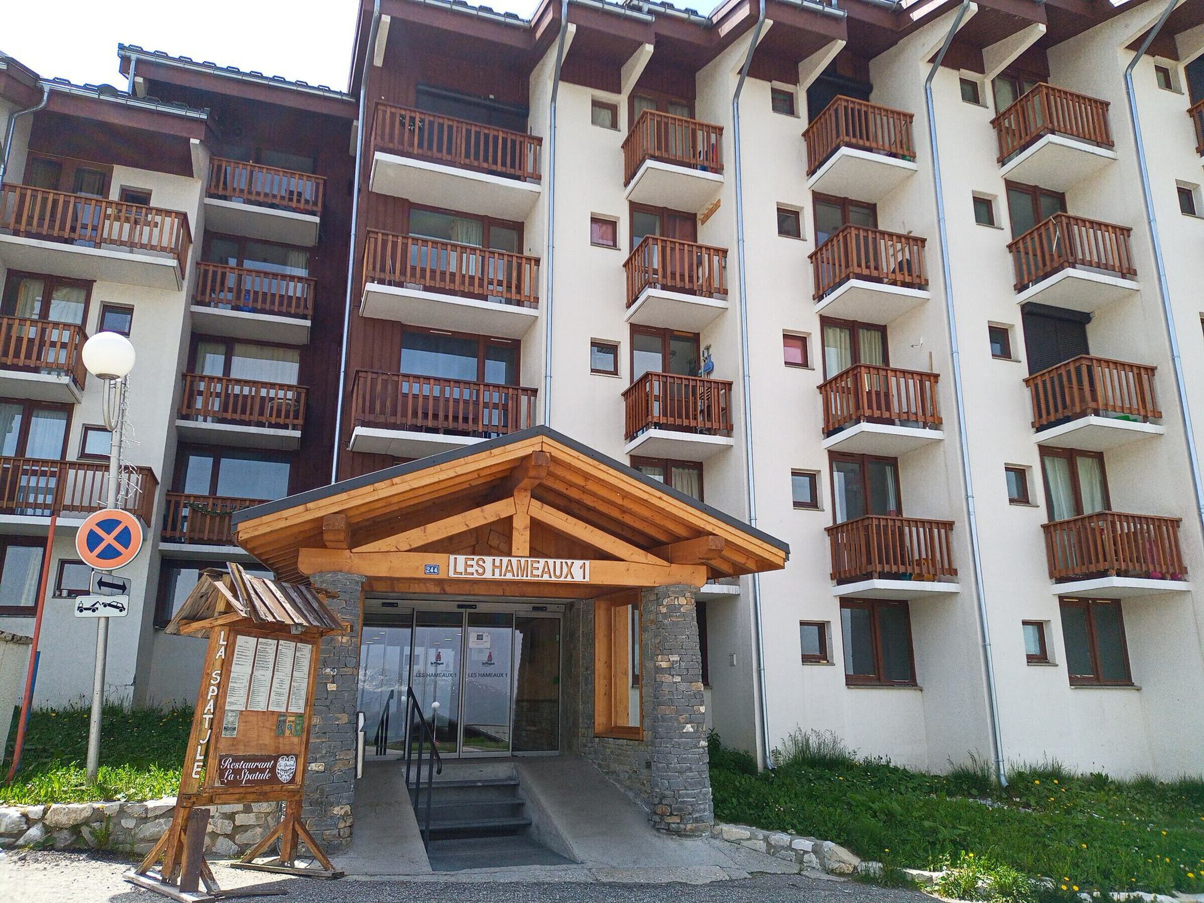Un hôtel à plusieurs étages, doté de balcons, d’une entrée en bois et d’une enseigne indiquant « LES HAMEAUX 1 ».