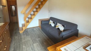 A compact living space with a wooden staircase, a grey sofa, and a wooden table.