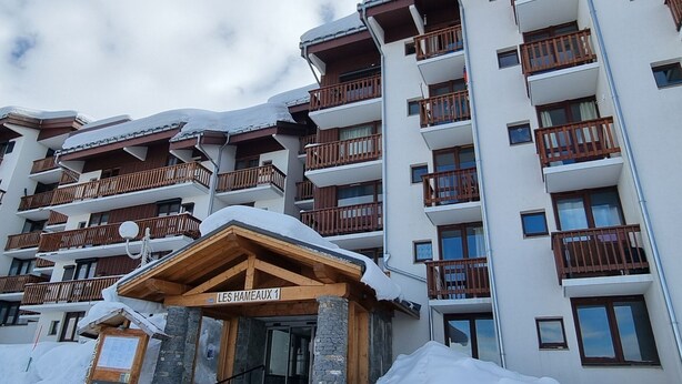 A multi-story hotel with balconies and a wooden entrance labeled "LES HAMEAUX 1".