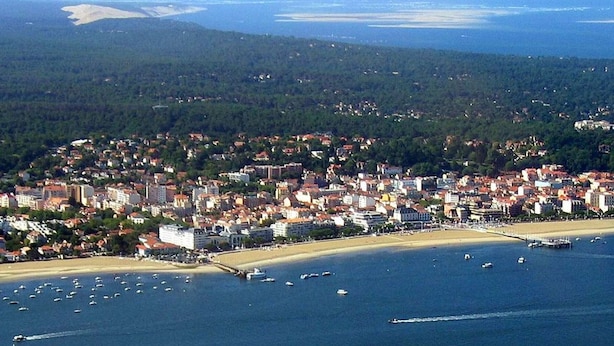 Vue aérienne d’une ville côtière, avec une zone densément peuplée, une plage et de nombreux bateaux sur l’eau.