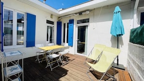 Un espace extérieur abrité, doté d’une terrasse en bois, d’une table jaune et de chaises blanches.
