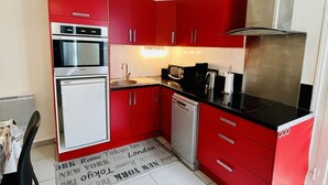 Une cuisine de taille réduite avec des meubles rouges, un réfrigérateur blanc, un four à micro-ondes, une machine à café et un lave-vaisselle.