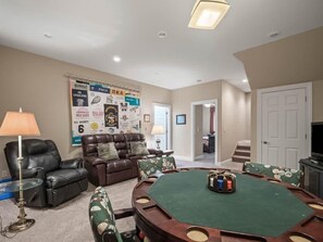 A living room with a green pool table, leather furniture, and a wall with various posters.