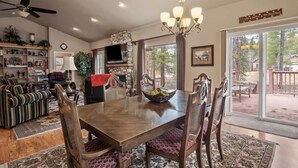 A dining area with a wooden table, chairs, a chandelier, and a stone fireplace.