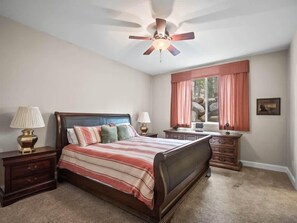 A bedroom with a bed, nightstands, a dresser, a ceiling fan, a window with curtains, and a framed picture on the wall.