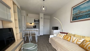 Un espace de vie compact comprenant un coin cuisine, un coin repas et un canapé agrémenté de coussins décoratifs.